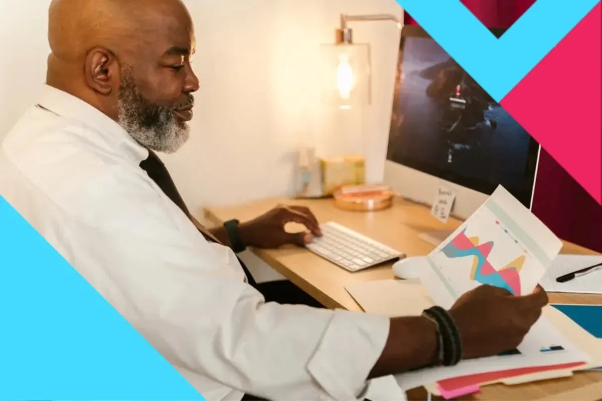 A man in a white shirt sits at a desk, examining a colorful graph. 