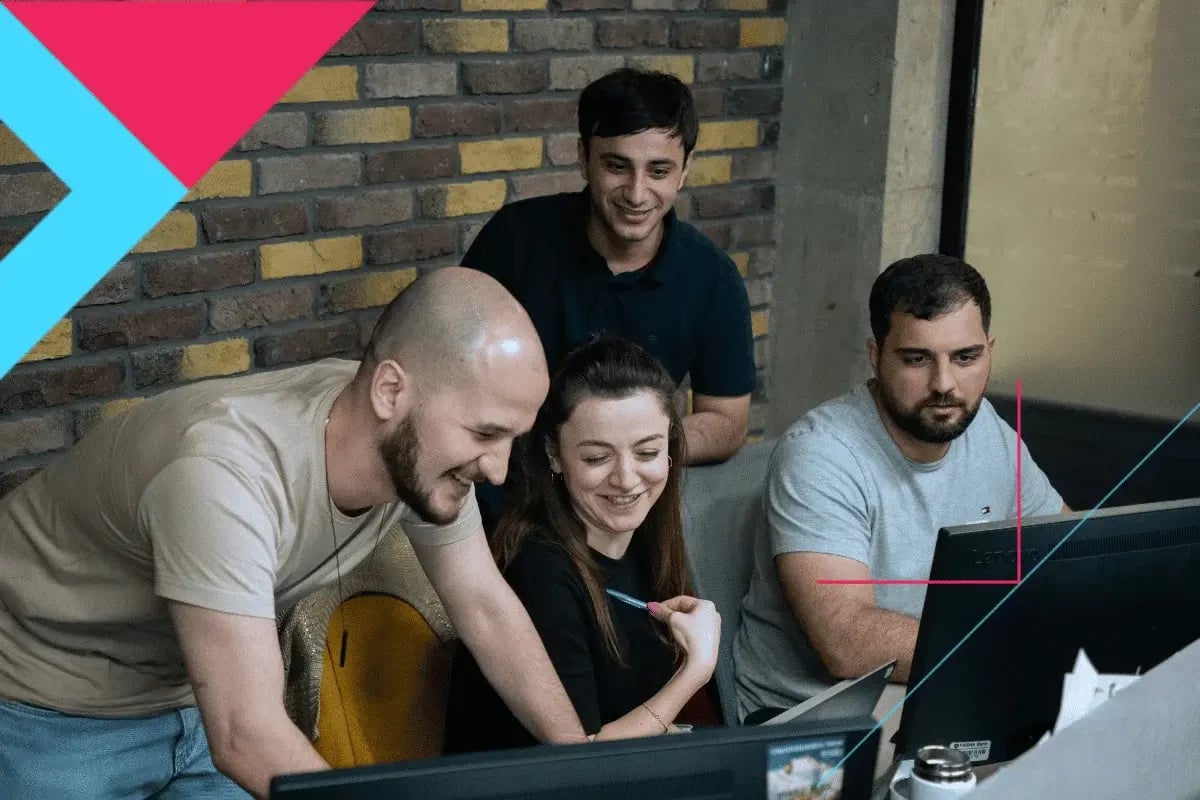 A group of four colleagues in a modern office, smiling and collaborating around a computer. The atmosphere is positive and focused.
