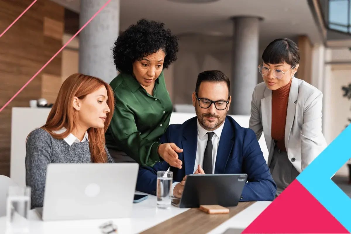 A diverse group of professionals collaborates around a tablet in a modern office setting, engaging in discussion and analysis.