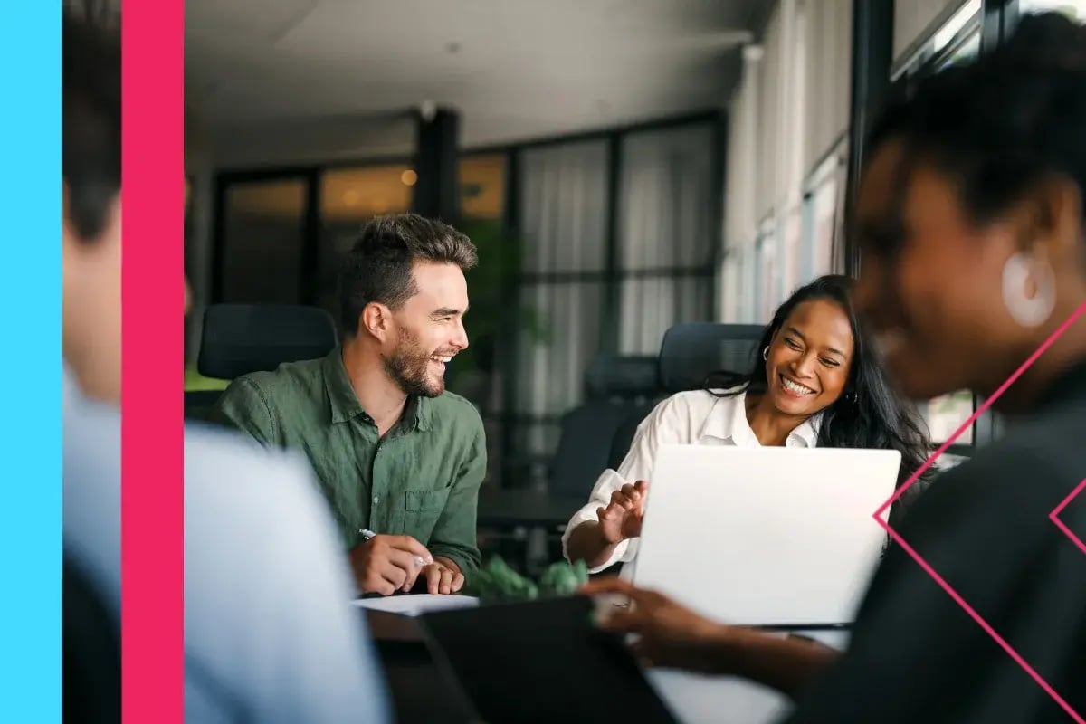 Diverse coworkers collaborate around a laptop in a bright office, smiling and engaged.