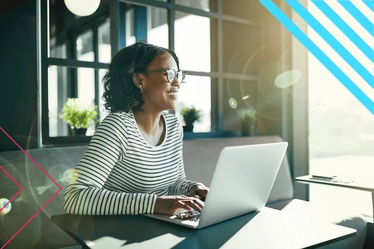 A person in glasses sits at a table, working on a laptop. 