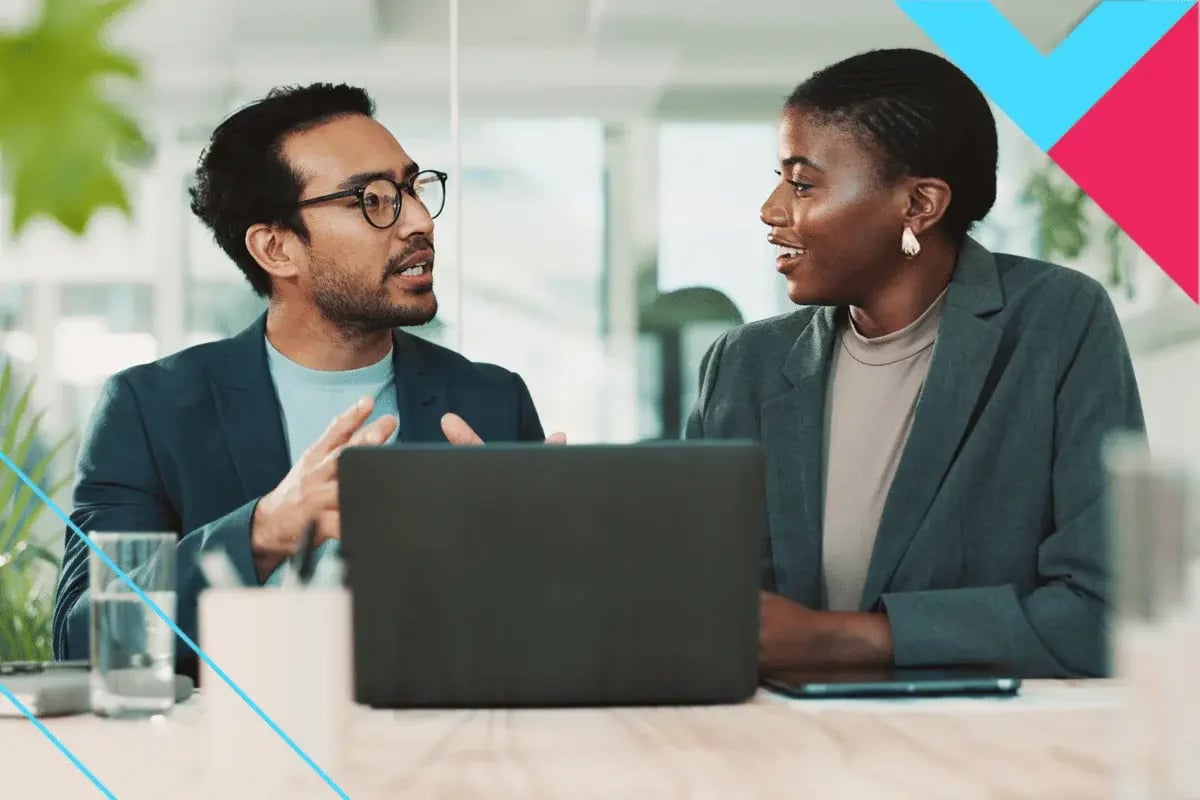 Two professionals engage in a lively desk discussion as a man gestures expressively to show engagement while a woman listens intently with focused attention.