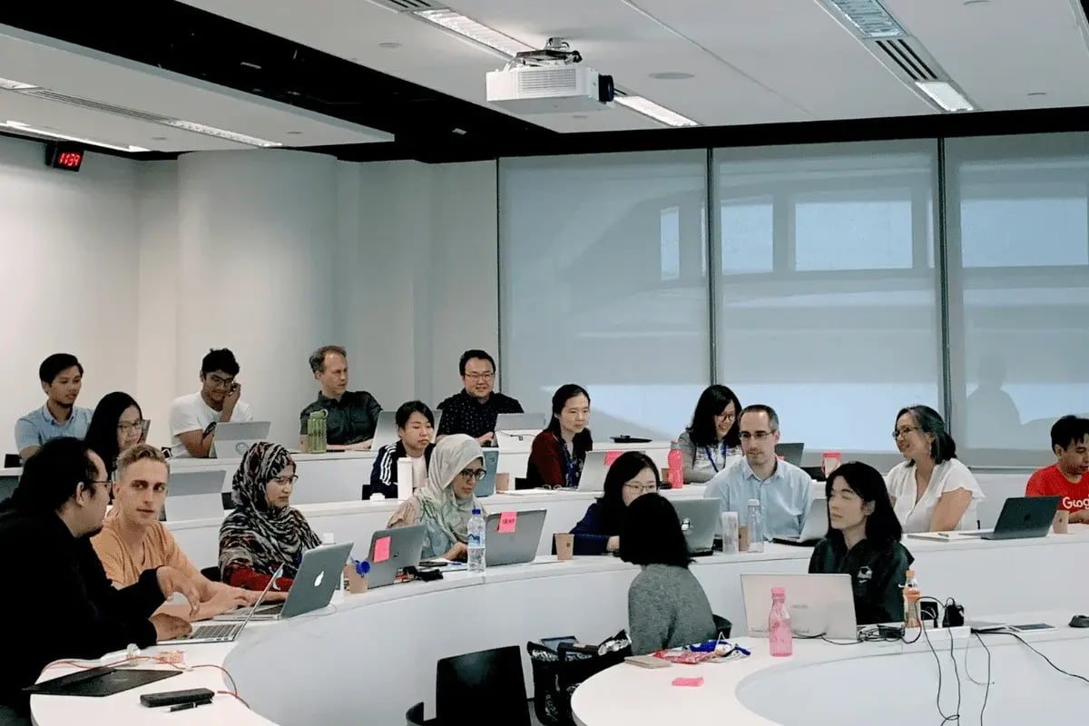 A diverse group of students attentively engaged in a classroom setting, using laptops and taking notes.