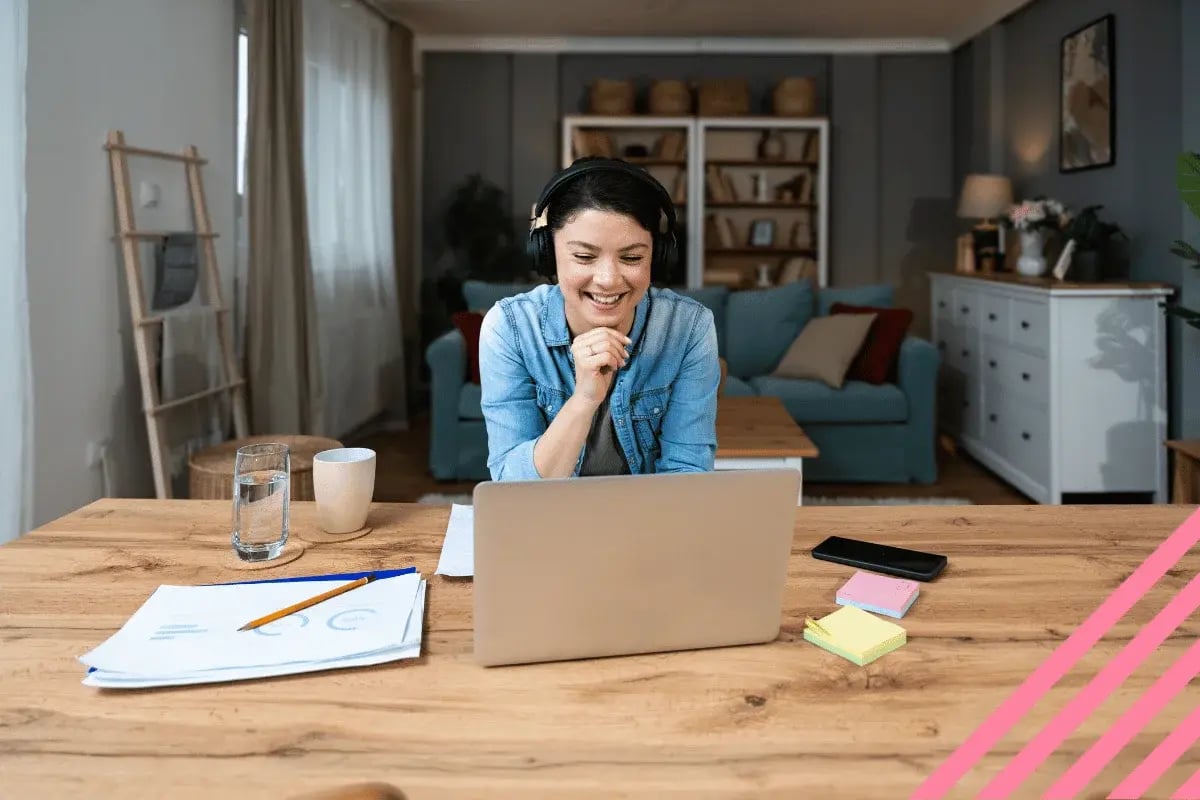 A woman in headphones smiles at a laptop in a modern living room. 