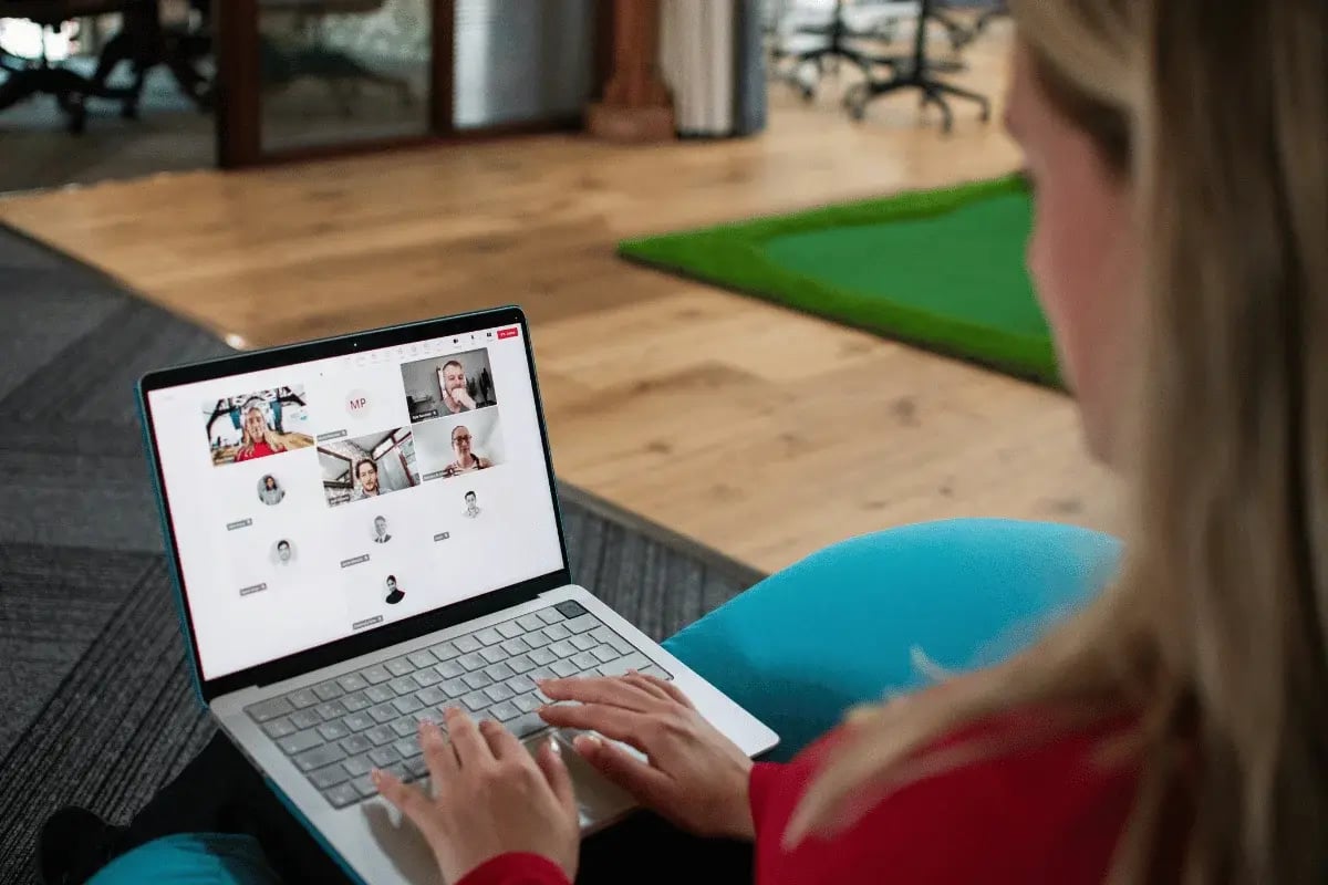 A person sits comfortably on a blue bean bag, engaged in a virtual meeting on a laptop displaying multiple participants.