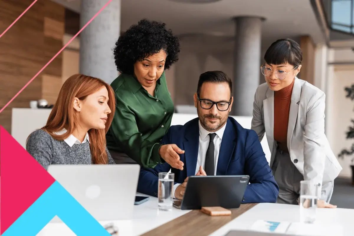 Four diverse professionals collaborate around a tablet in a modern office. They appear engaged and focused, fostering a sense of teamwork and innovation.