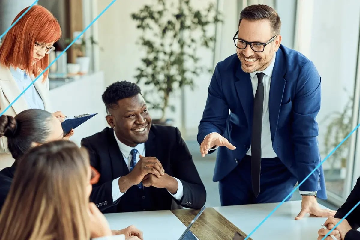 Diverse professionals collaborating in a bright office meeting, with a smiling man in a blue suit leading discussion.