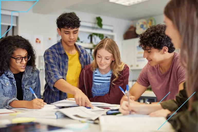 A group of five diverse students collaborates around a table, discussing and pointing at textbooks. The atmosphere is focused and cooperative.