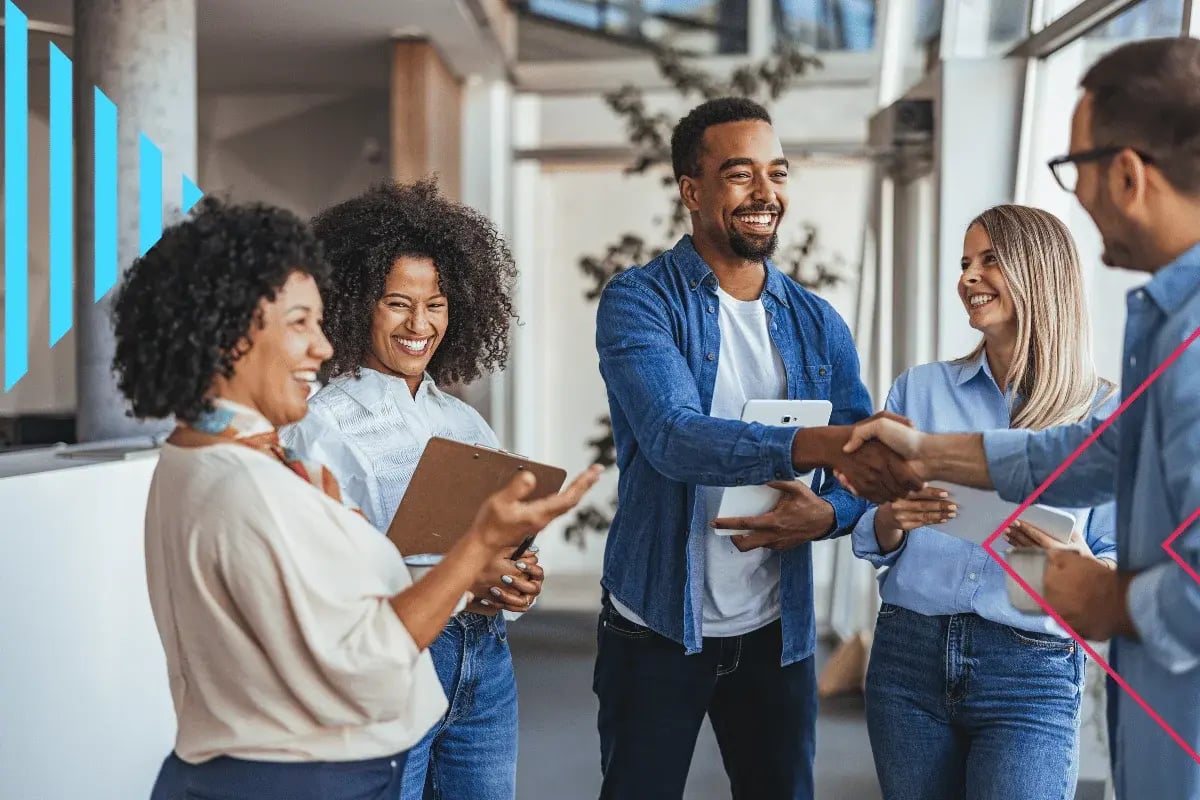 A diverse group of four people in casual attire are smiling and shaking hands in a modern office. The atmosphere is positive and collaborative.