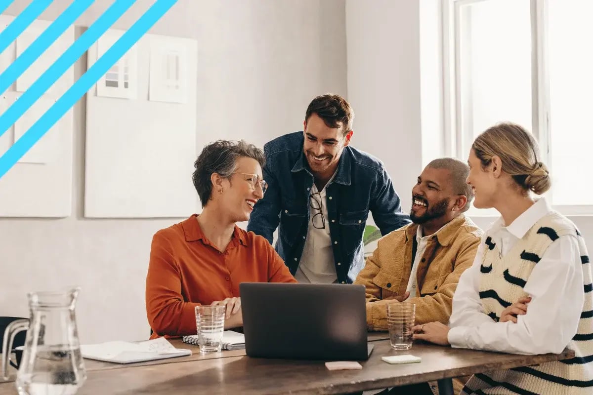 A diverse group of four people smiling and collaborating around a laptop in a modern office.