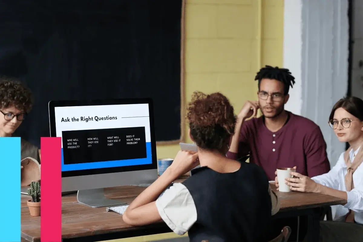 A diverse group of four people sit around a table with a computer displaying "Ask the Right Questions." They appear engaged and thoughtful.