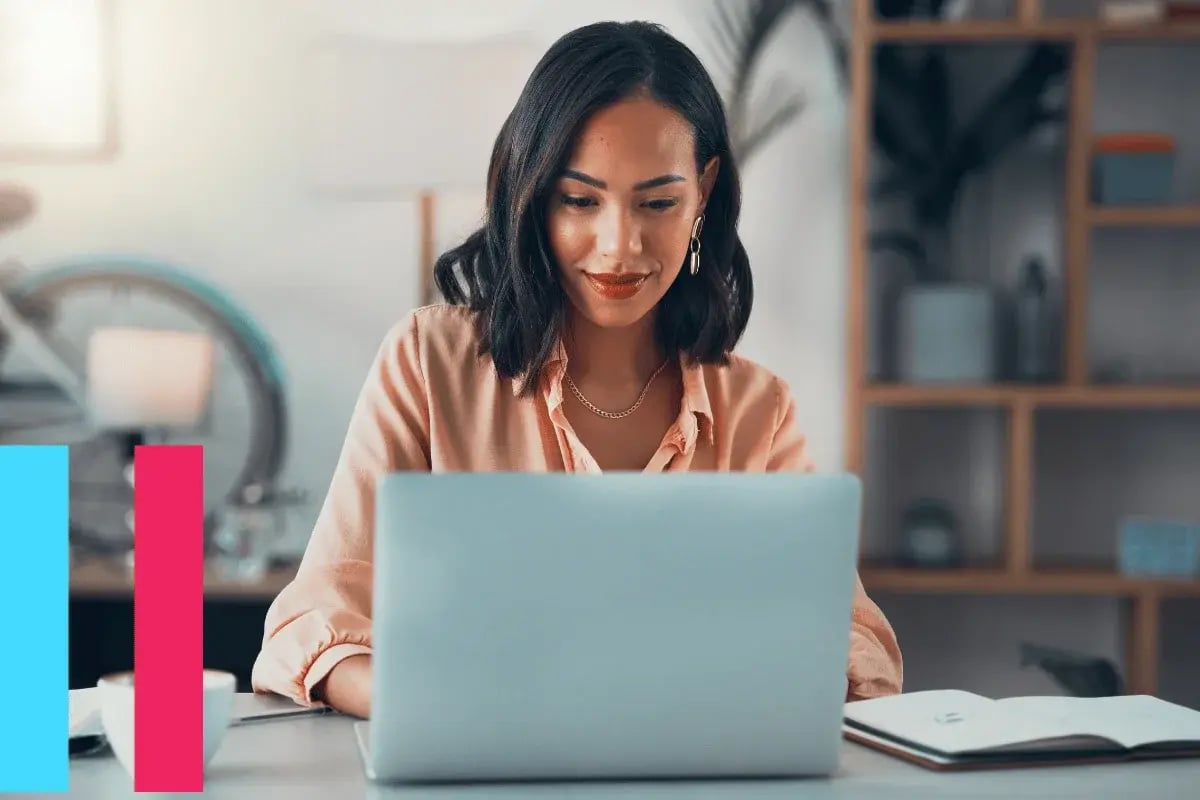 A woman sits at a desk in a stylish office, focused on her laptop. Her expression is calm and engaged. An open notebook and bookshelf are in the background.