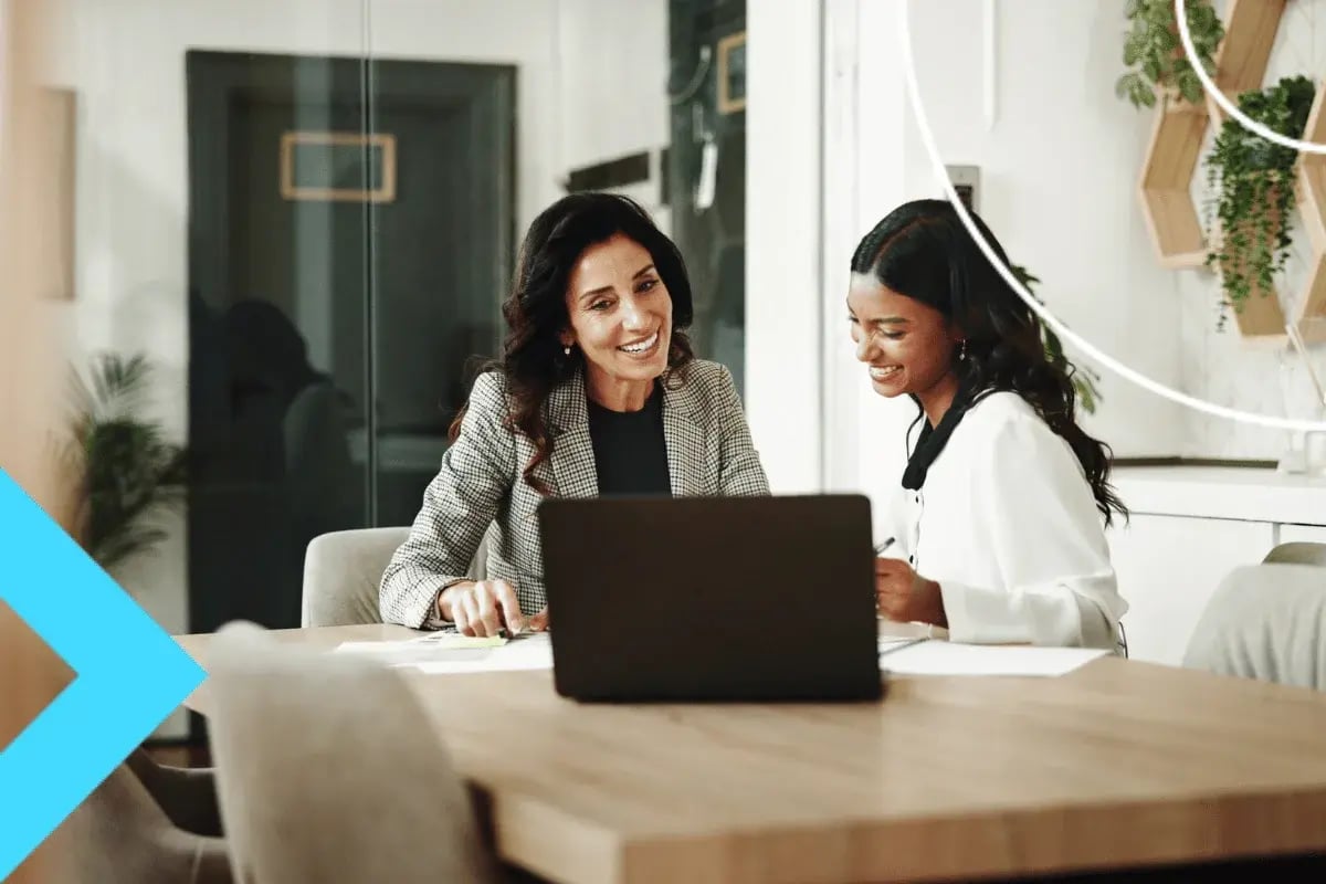 Two professionals collaborating on a laptop while reviewing documents at a conference table.