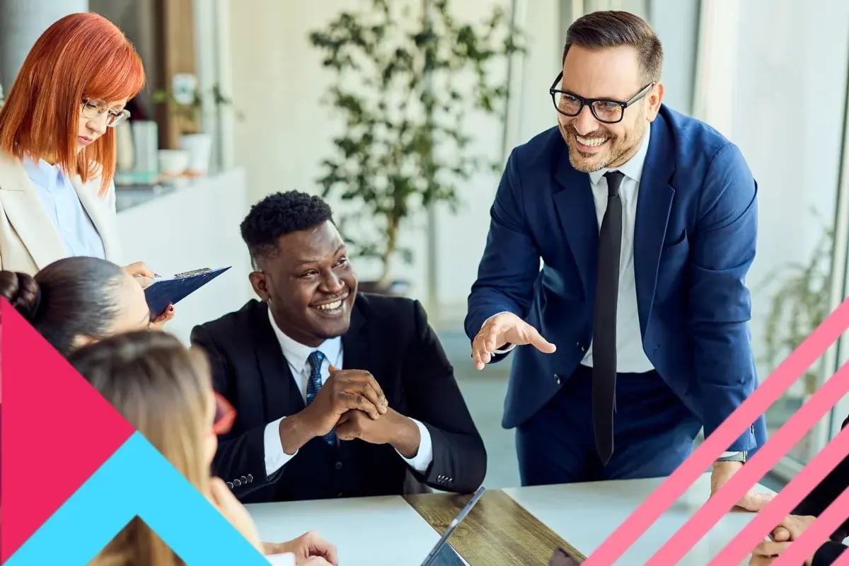 A diverse group of people in business attire sits around a table, smiling and discussing.