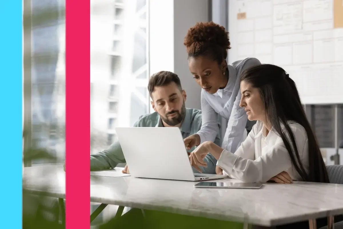 Three colleagues collaborating at a modern office table, focusing on a laptop.