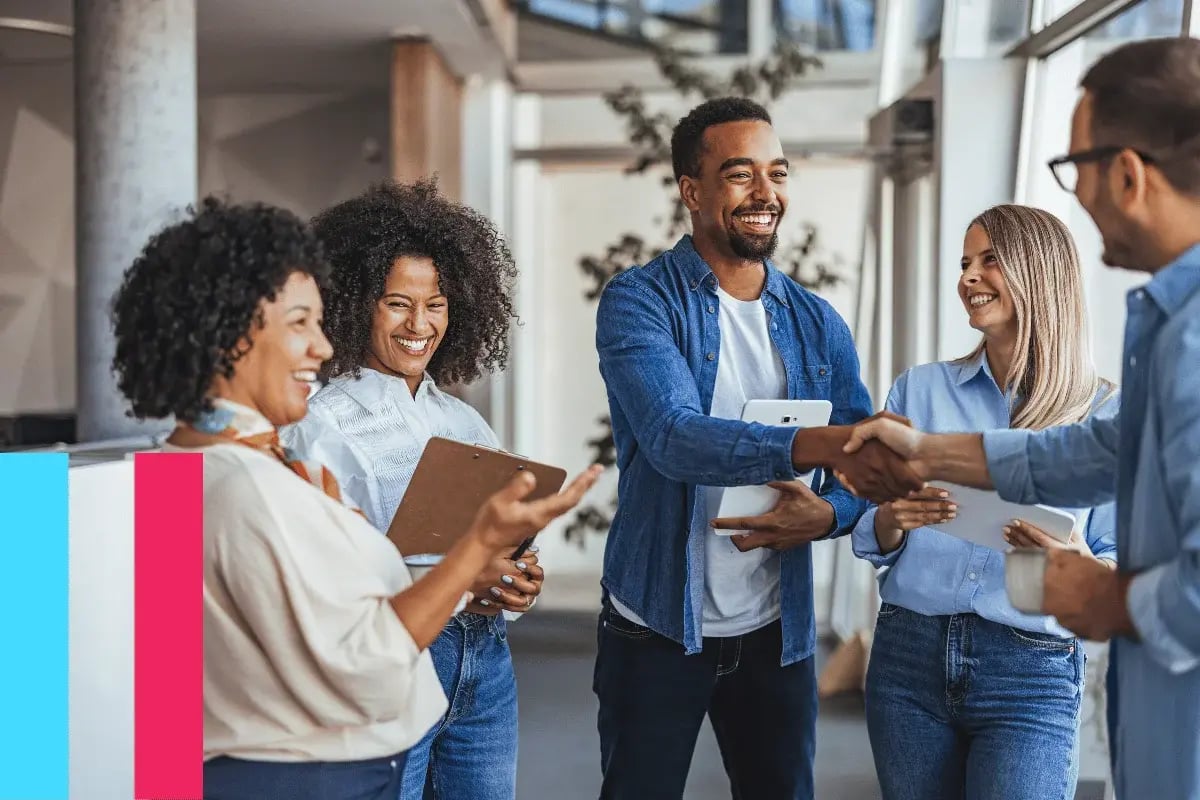 A diverse group of four people in business casual attire engage in a cheerful conversation in an office.