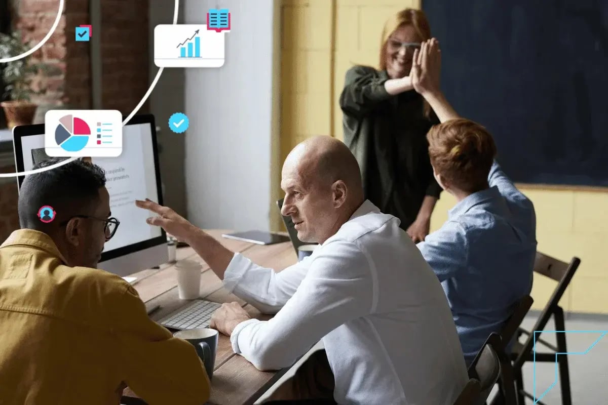 A group in an office is discussing work at a table, with colorful data icons floating nearby. Two people celebrate with a high-five in the background.