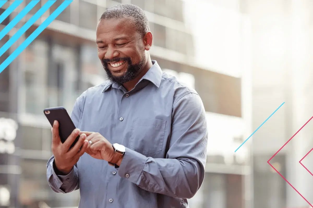 Smiling man in a blue shirt uses a smartphone outside, the atmosphere feels modern and positive.