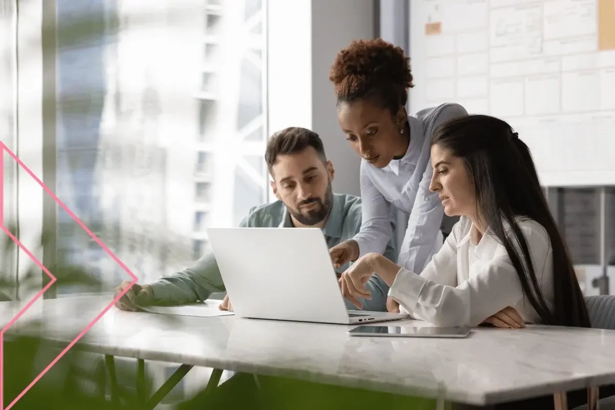 A diverse group of professionals collaborates around a laptop in a bright, modern office workspace.