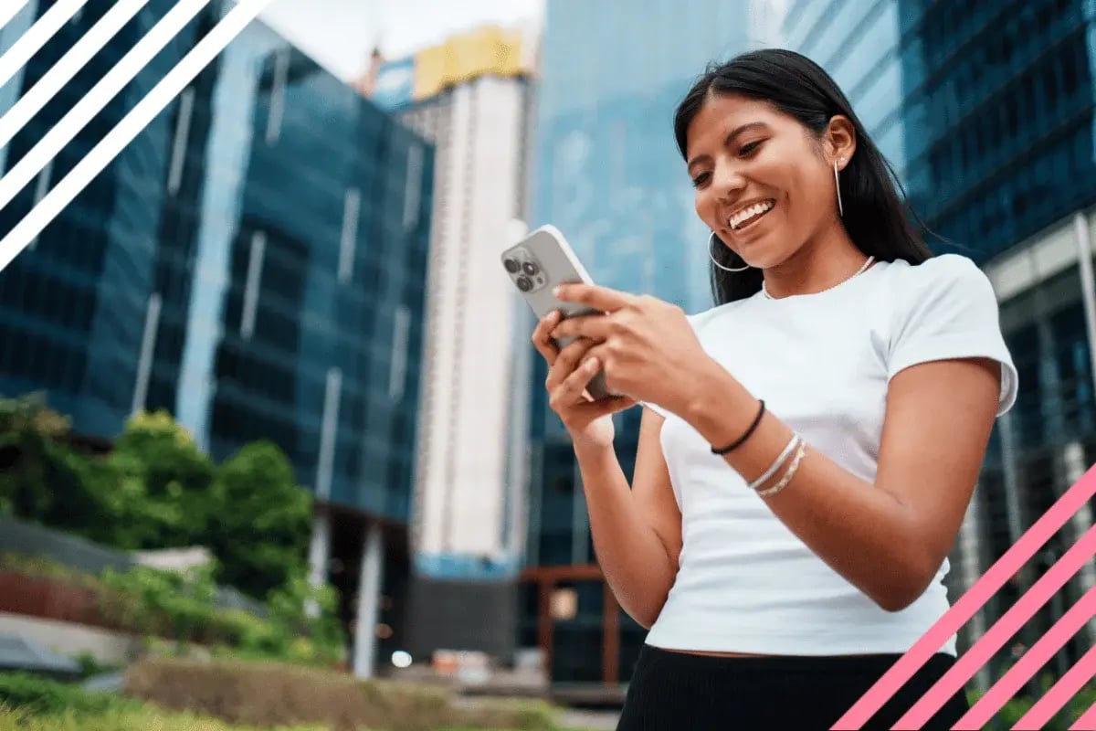 Happy young woman in a white top smiling at her phone in a modern urban setting with glass buildings. 