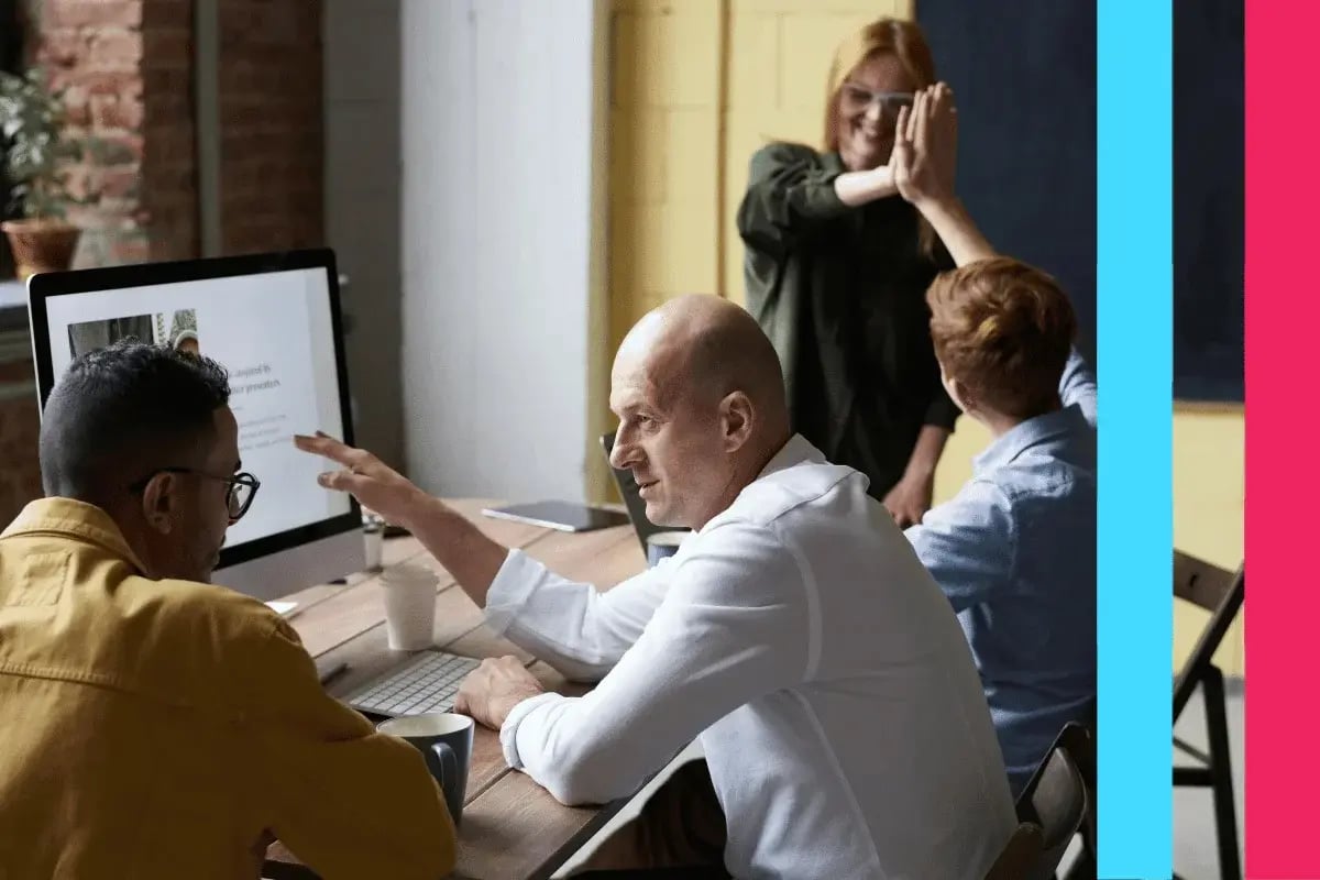 A diverse group in a modern office collaborates around a computer. 