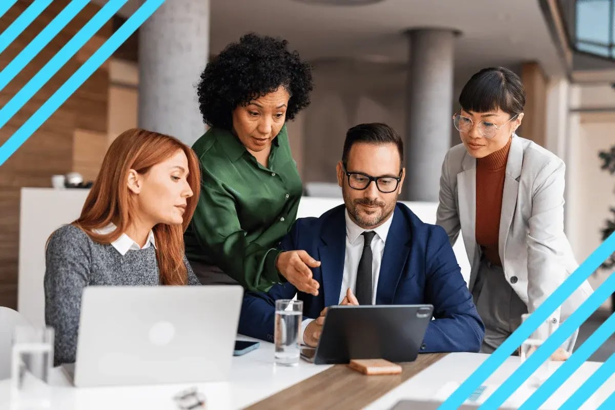 Four business professionals collaborating around a tablet in a bright modern office, focused on teamwork and strategy.