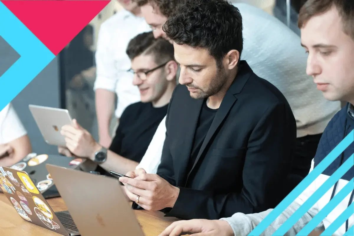 A group of focused young professionals collaborating around a table with laptops and tablets.